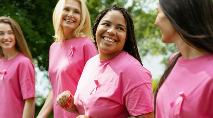 Group of women smiling, wearing pink and breast cancer ribbons.