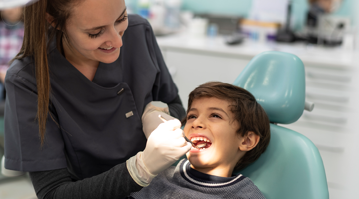 A dental assistant checks the mouth of a adolescent patient.