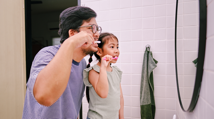 Father and daughter brushing their teeth in the bathroom.