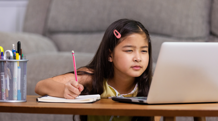 Child taking notes from her computer to a notebook.