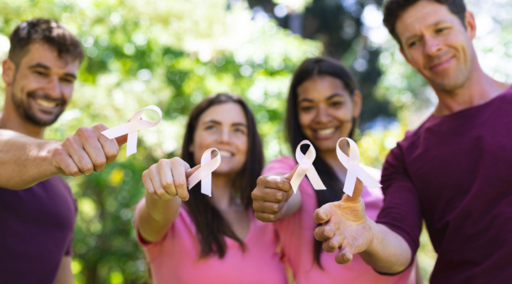 Group of friends smiling and holding up Breast Cancer Awareness ribbons.
