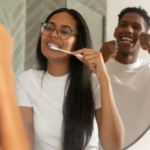 One person brushing their teeth in the mirror and another person flossing in the mirror.