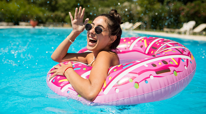 Person swimming and smiling in the pool with sunglasses on.