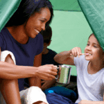 Child brushing their teeth in a tent with her mom.
