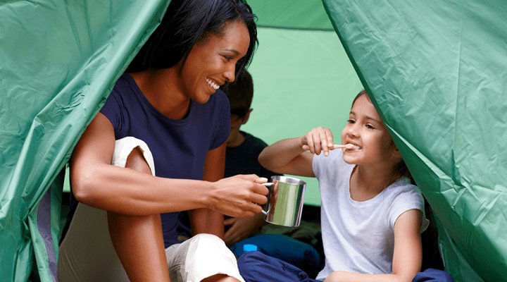 Child brushing their teeth in a tent with her mom.