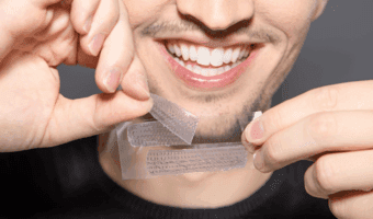 Person smiling and holding teeth whitening strips.
